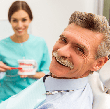 An older man sitting in a dental chair and smiling at the camera