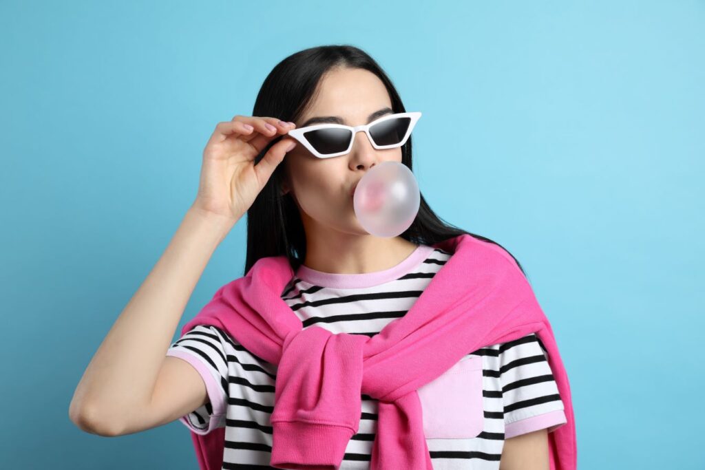 A woman in sunglasses blowing a bubblegum bubble.